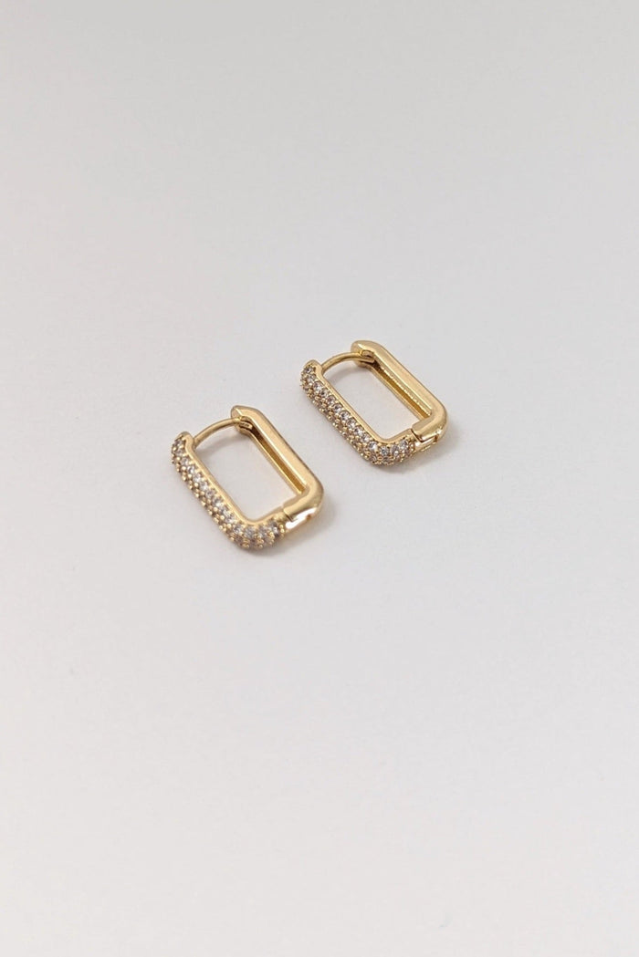 A pair of gold-colored rectangular pave huggie earrings on a white background