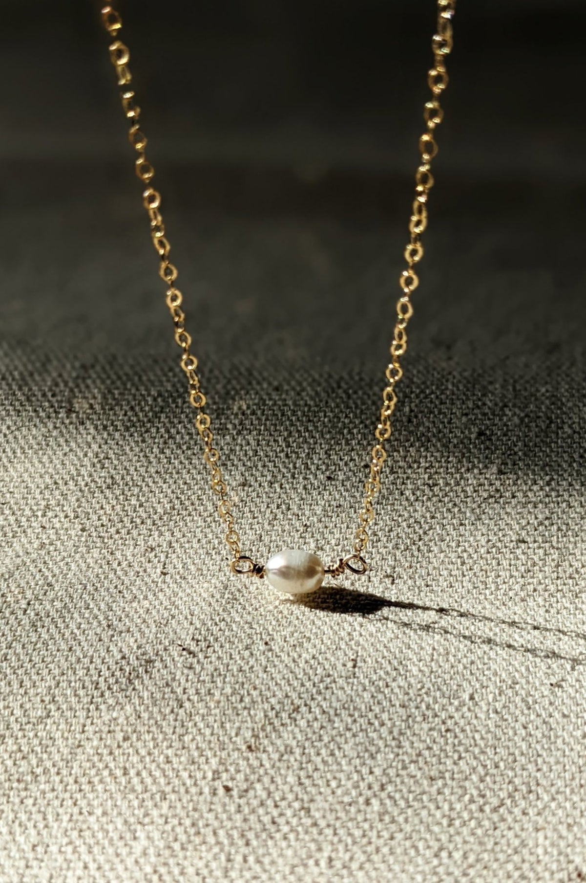 A gold-filled chain necklace with a classic design, featuring a single freshwater pearl pendant.