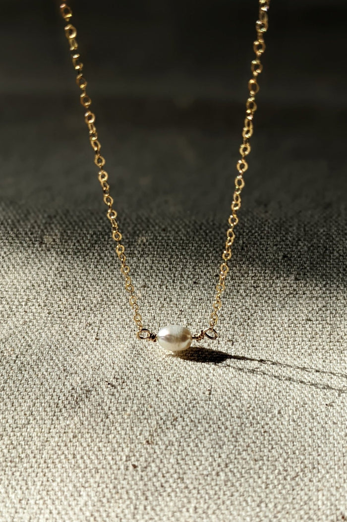 A gold-filled chain necklace with a classic design, featuring a single freshwater pearl pendant.