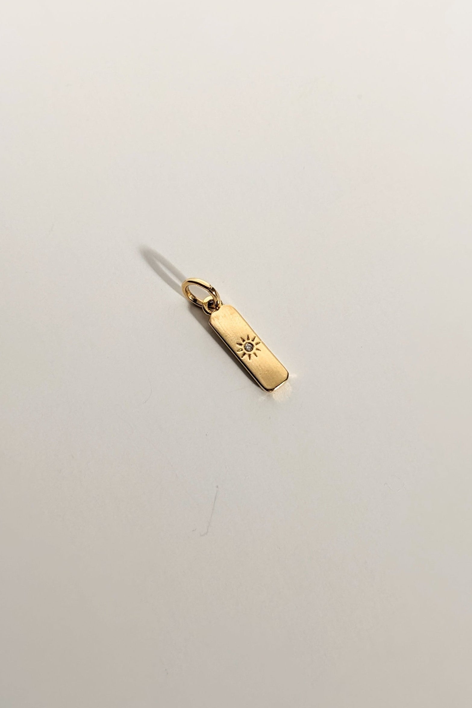 Gold pendant with engraved design on a light gray background