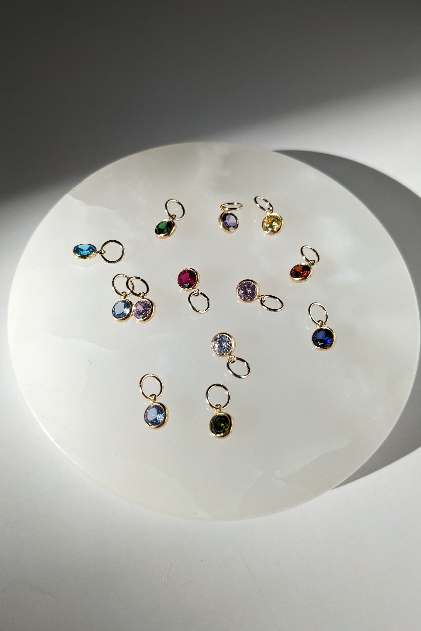 Collection of small gemstone charms on a white plate with a gray background
