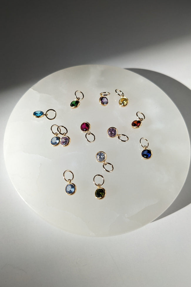 Collection of small gemstone charms on a white plate with a gray background