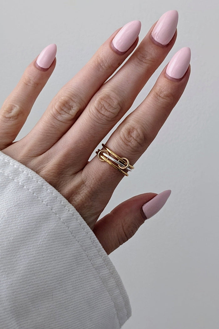 Hand with pink nails and gold rings on a plain background