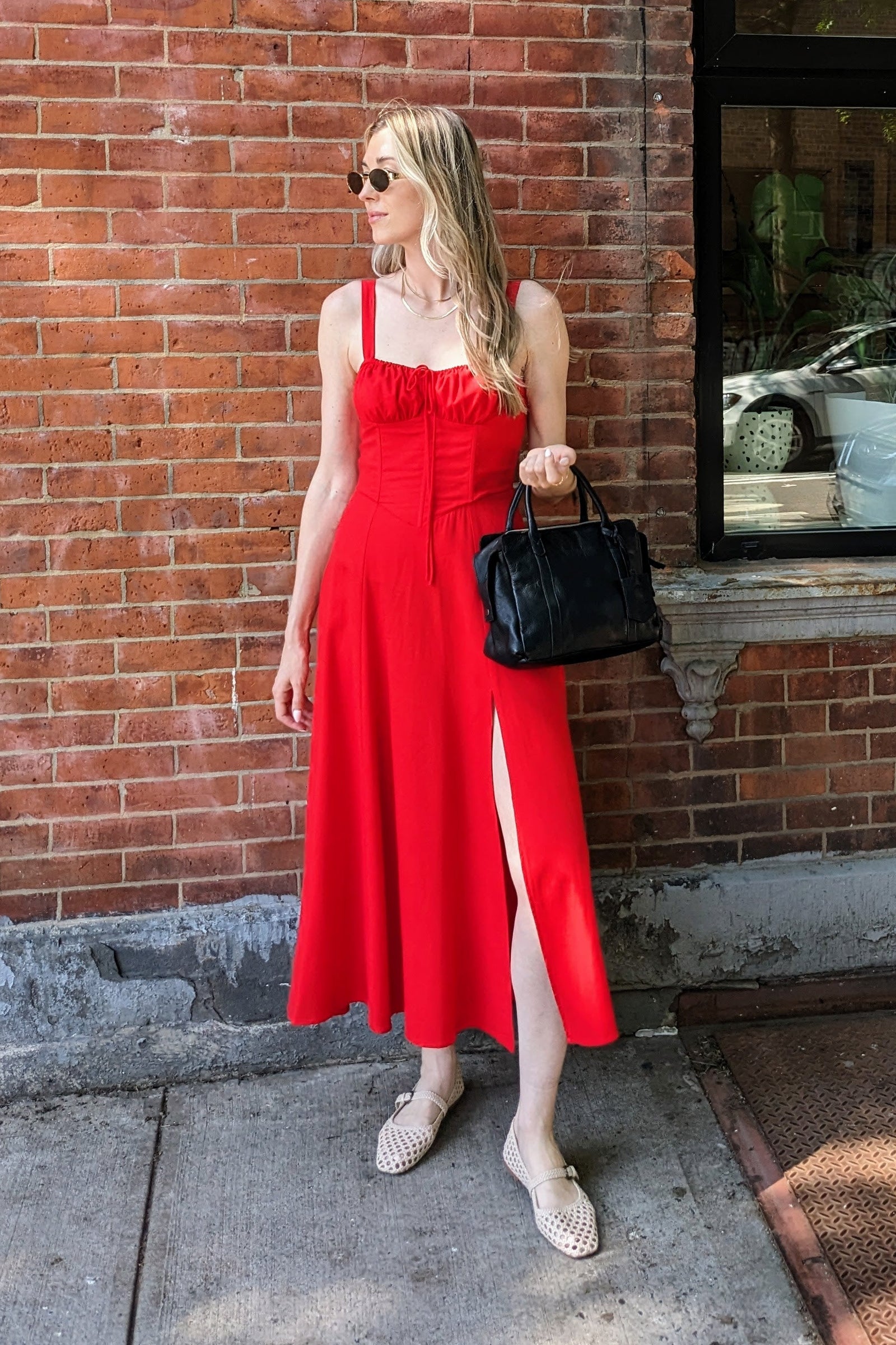 Woman in a red dress standing against a brick wall with a window.