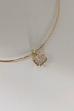 A delicate gold bangle bracelet with a small hexagonal pendant featuring a textured, diamond-like clear stone in a gold bezel setting, displayed on a neutral light gray background.