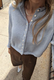 A person wearing a light blue knit button-front cardigan with brown pants, standing outdoors on a concrete sidewalk.