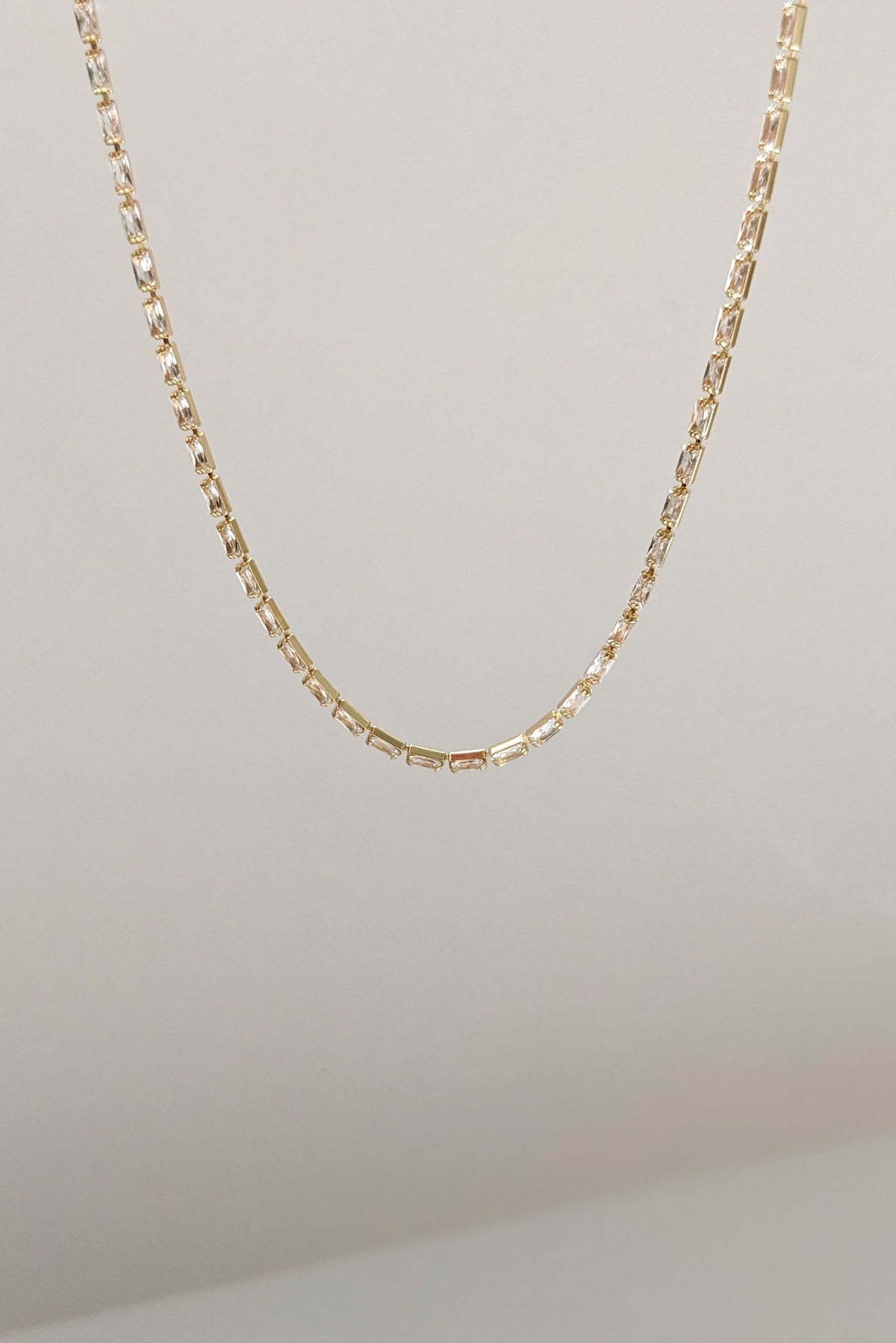 A delicate gold chain necklace with a textured, geometric link design, shown hanging against a plain off-white background.