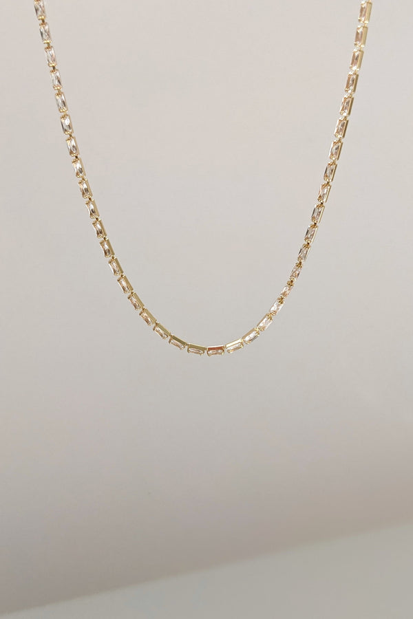 A delicate gold chain necklace with a textured, geometric link design, shown hanging against a plain off-white background.
