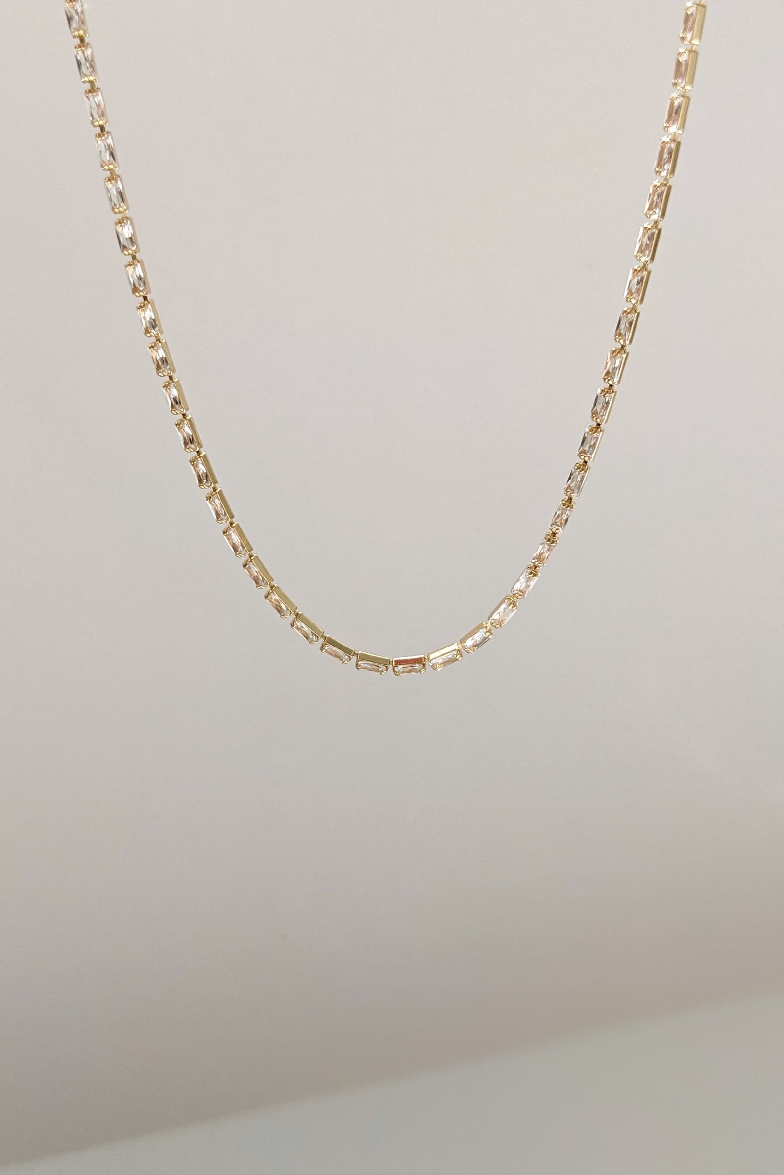 A delicate gold chain necklace with a textured, geometric link design, shown hanging against a plain off-white background.