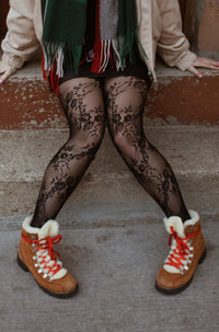 Person wearing a plaid scarf, beige jacket, black patterned tights, and brown boots on stone steps.