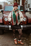 Person wearing a colorful scarf, beige coat, and patterned leggings standing in front of a red Jeep.