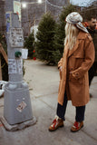 Person in a tan coat standing next to a parking meter with Christmas trees in the background