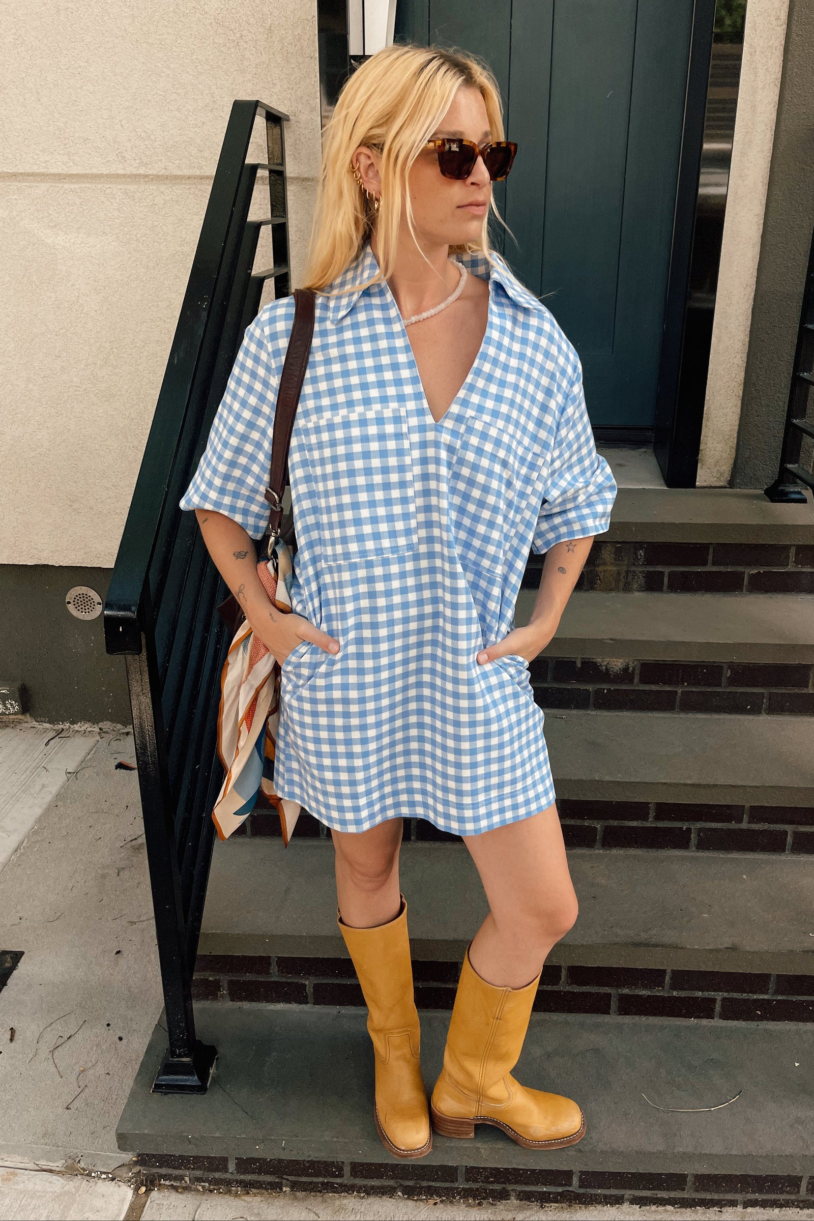 Woman wearing a blue checkered dress and yellow boots standing on steps.