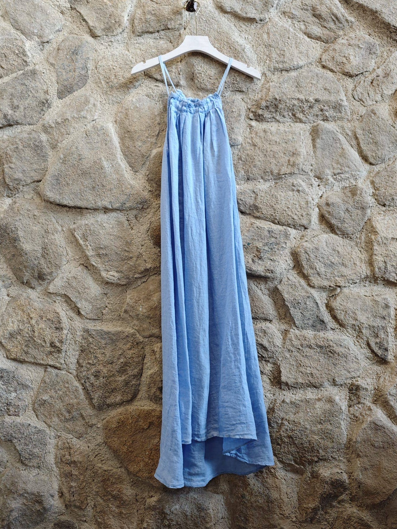 Light blue dress hanging on a hanger against a stone wall