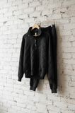 Black quilted jacket and pants hanging on a white brick wall.