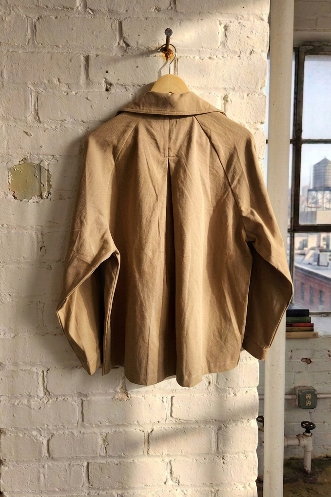 Brown jacket hanging on a hook against a white brick wall with a cityscape view.