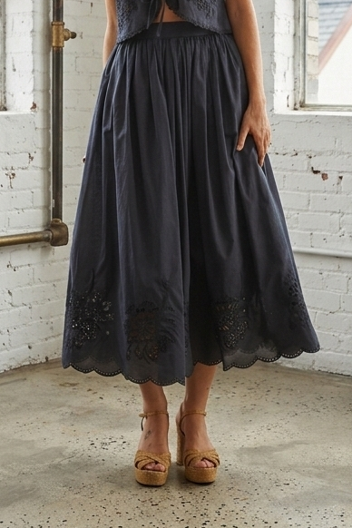Woman in a navy dress standing in a room with large windows and white brick walls.