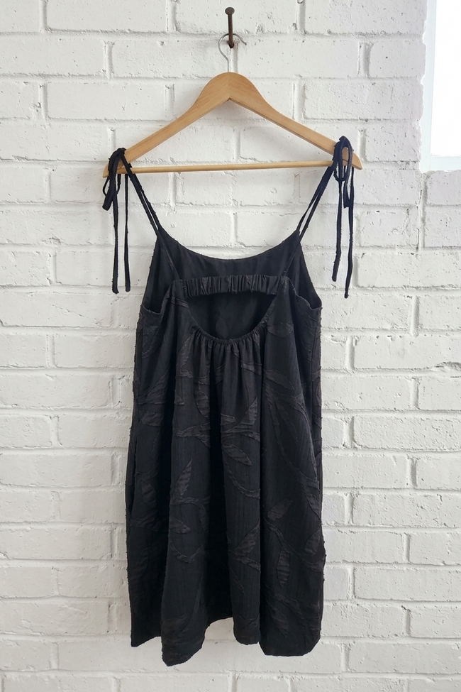 Black slip dress on a wooden hanger against a white brick wall
