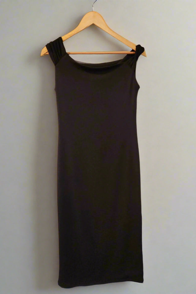 Black sleeveless dress on a hanger against a white wall.