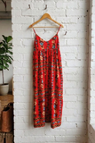 Red floral dress hanging on a wooden hanger against a white brick wall.