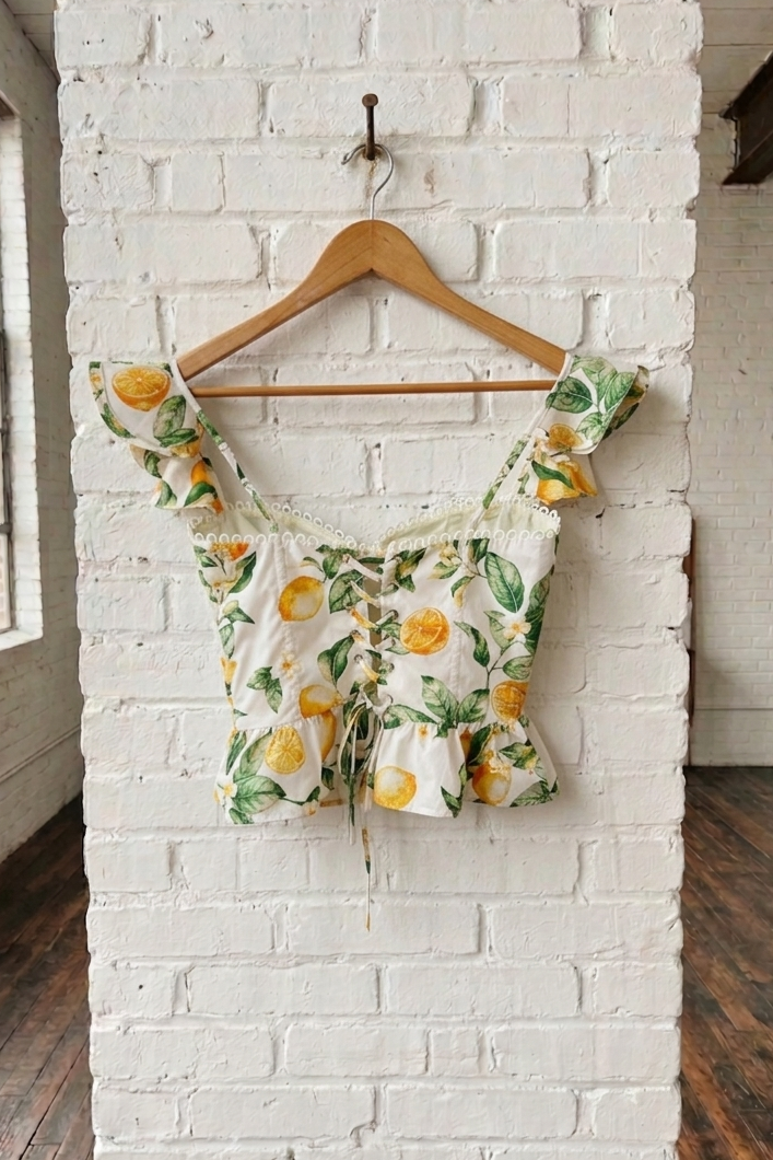 Floral top with lemon pattern on a wooden hanger against a white brick wall.
