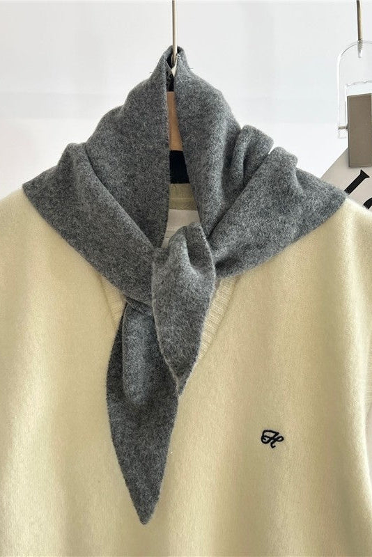 Gray scarf draped over a light yellow vest with a white shirt underneath on a plain background.