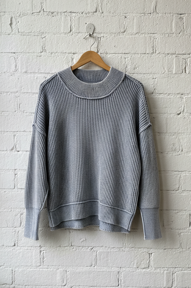 blue ribbed sweater hanging on a wooden hanger against a white brick wall.