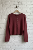 Maroon cardigan on a wooden hanger against a white brick wall