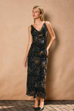 Woman wearing a black floral velvet dress against a beige wall.