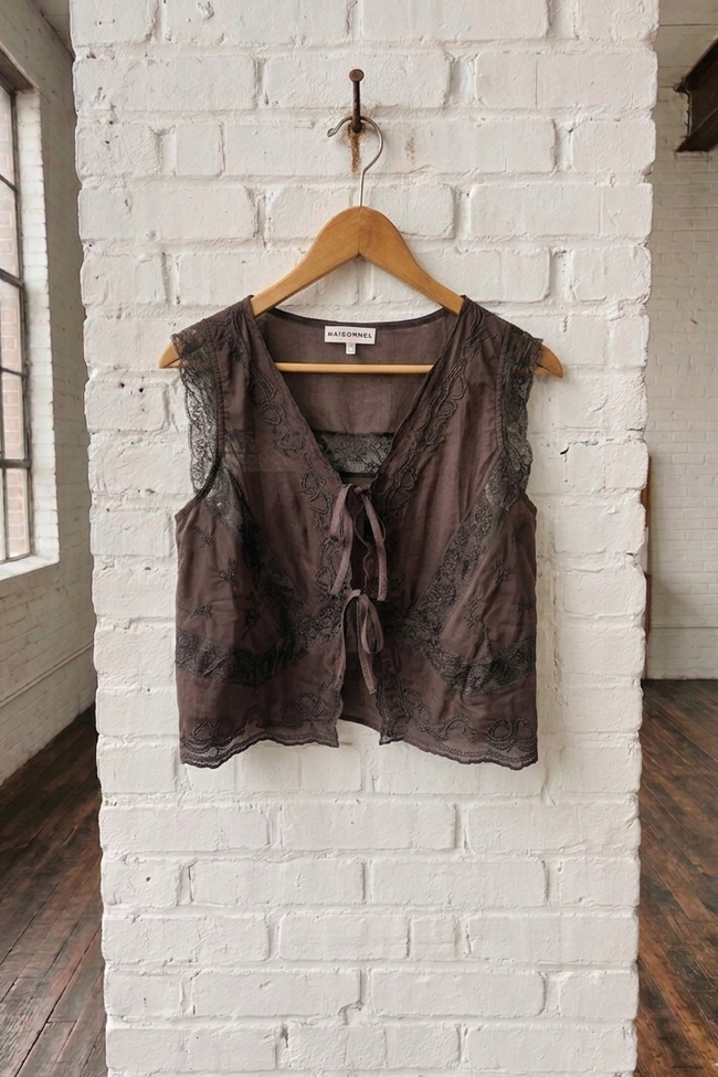 Brown sleeveless top on a wooden hanger against a white brick wall.