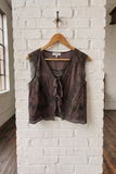 Brown sleeveless top on a wooden hanger against a white brick wall.