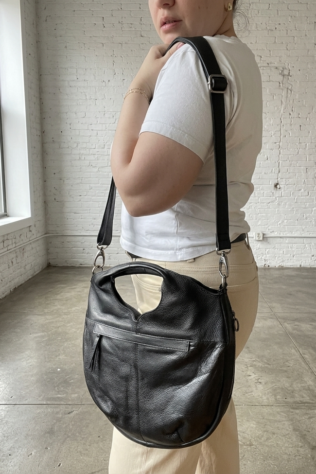 Person holding a black leather handbag in an indoor setting with white brick walls.
