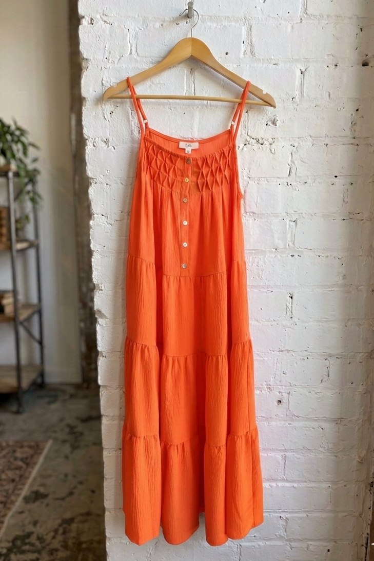 Orange dress hanging on a wooden hanger against a white brick wall.