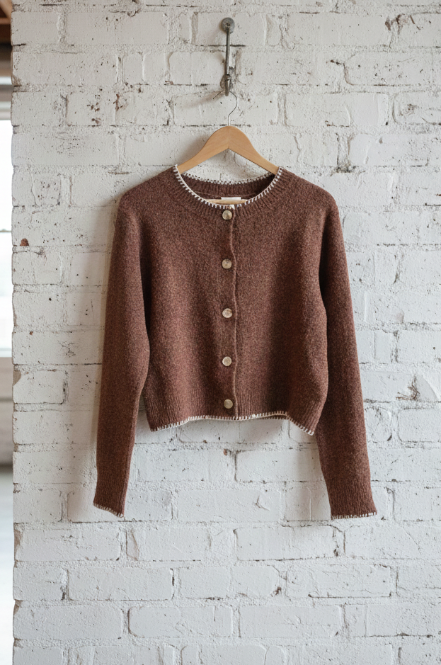 Brown cardigan on a hanger against a white brick wall