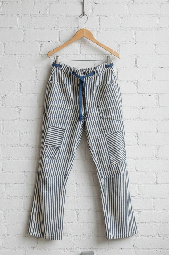Striped pants hanging on a wooden hanger against a white brick wall.