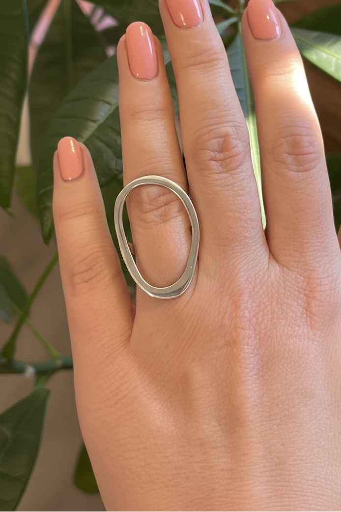 Hand wearing a silver ring with a plant in the background