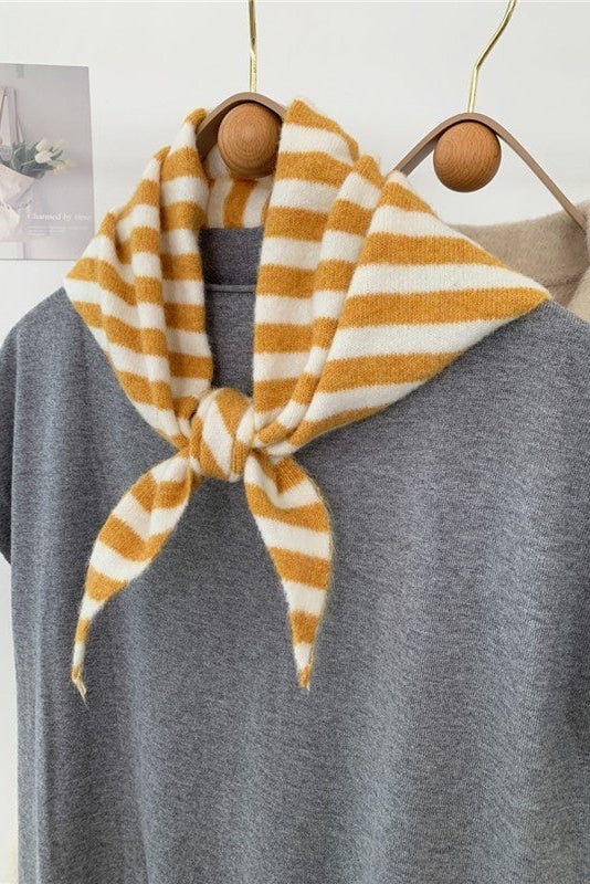 Yellow and white striped scarf tied around a gray sweater on a hanger against a light background.