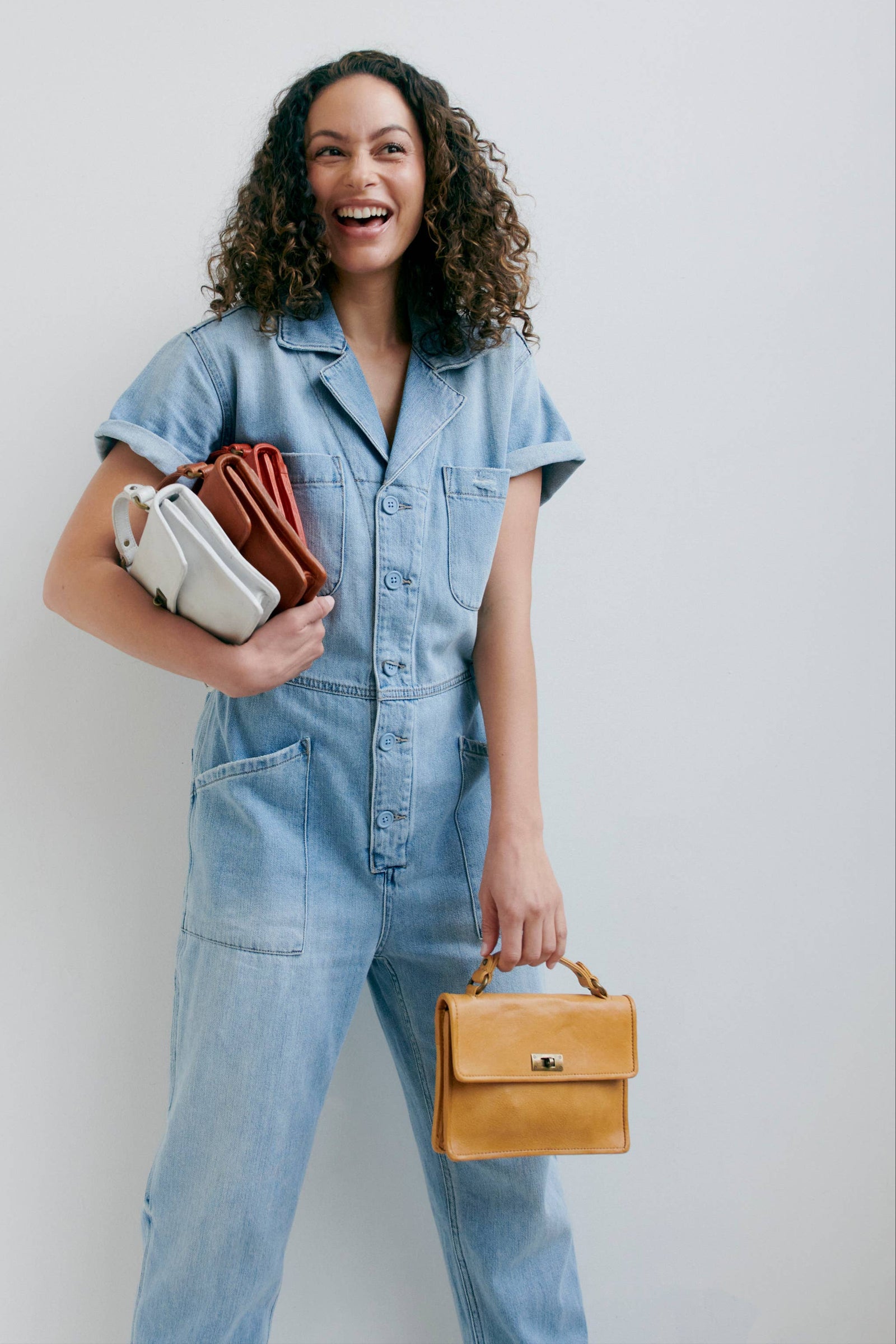 Woman in a denim outfit holding bags against a plain background