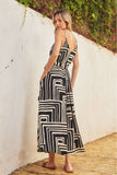 Woman wearing a black and white patterned dress standing against a white wall with greenery.