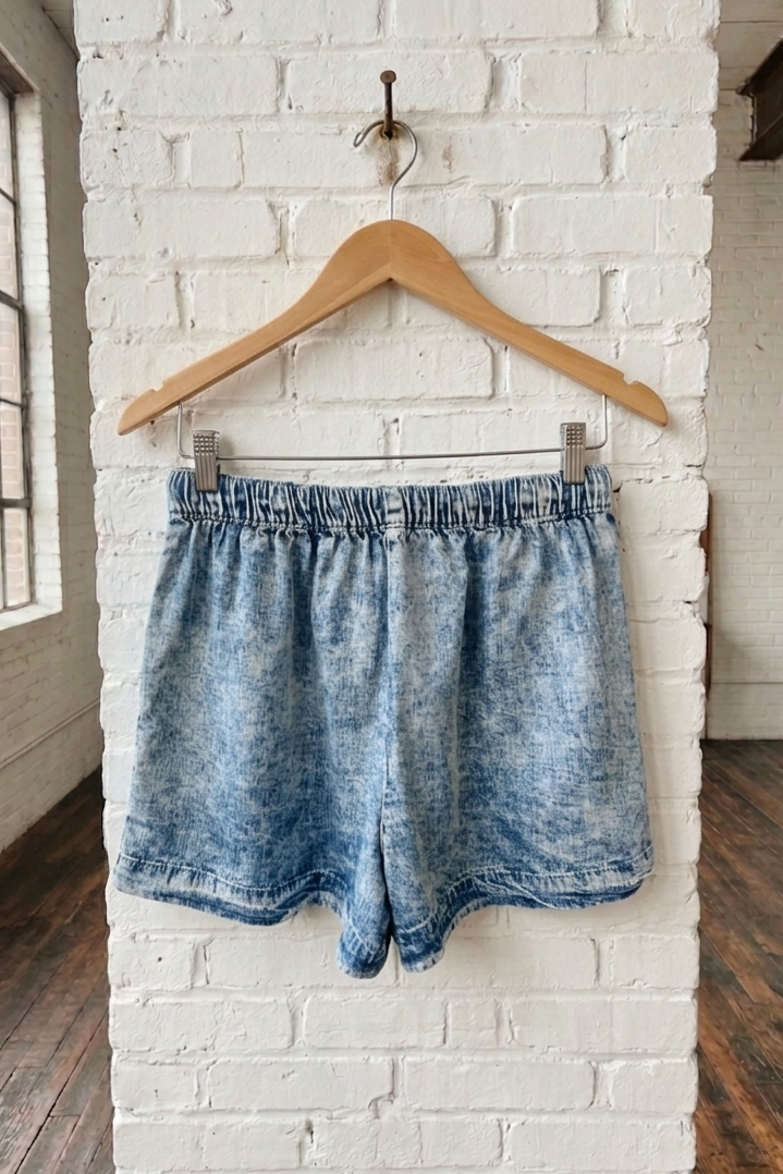 Blue denim shorts on a wooden hanger against a white brick wall.
