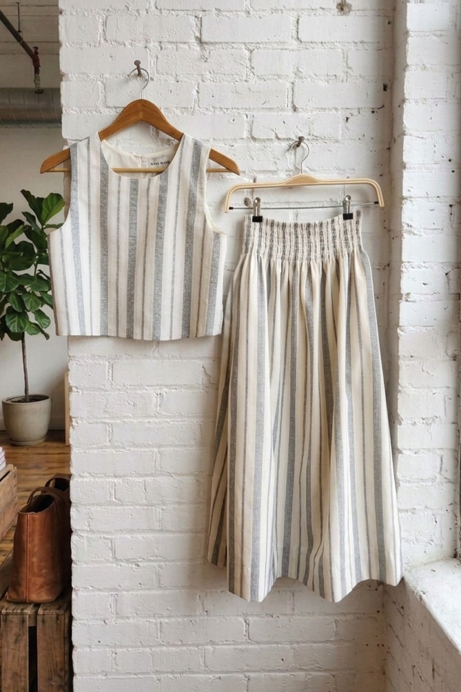 Striped top and skirt set hanging on a rack against a white brick wall.