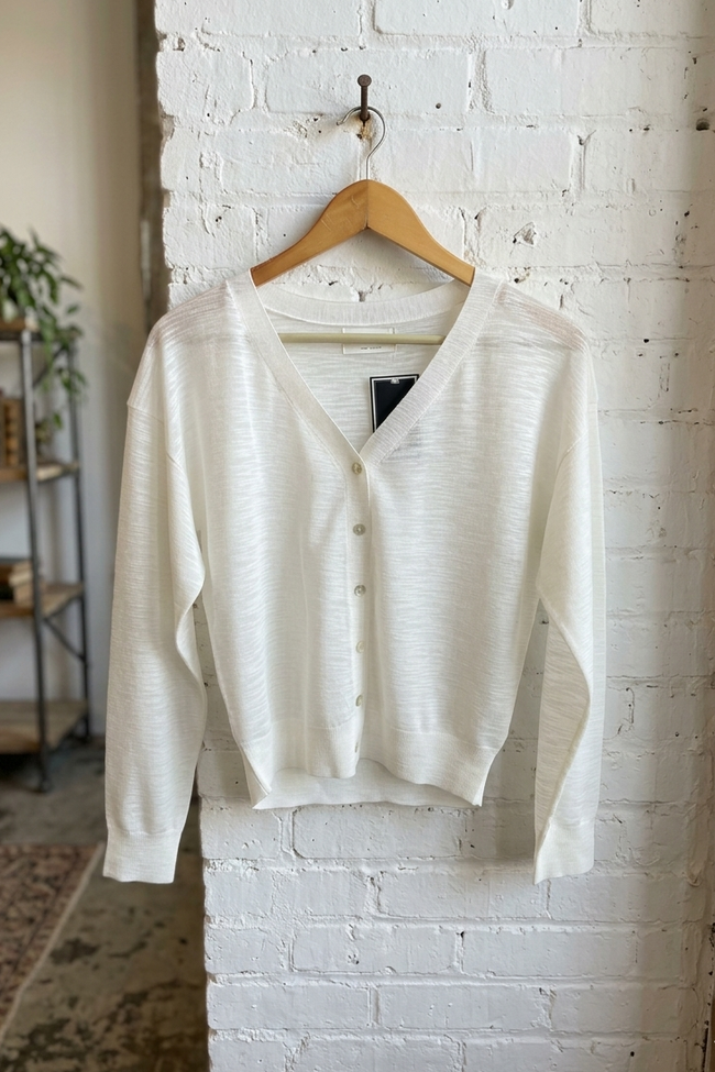 White cardigan on a wooden hanger against a white brick wall.