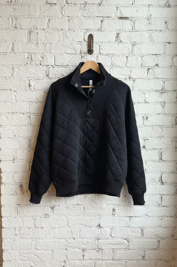 Black quilted jacket hanging on a hook against a white brick wall.