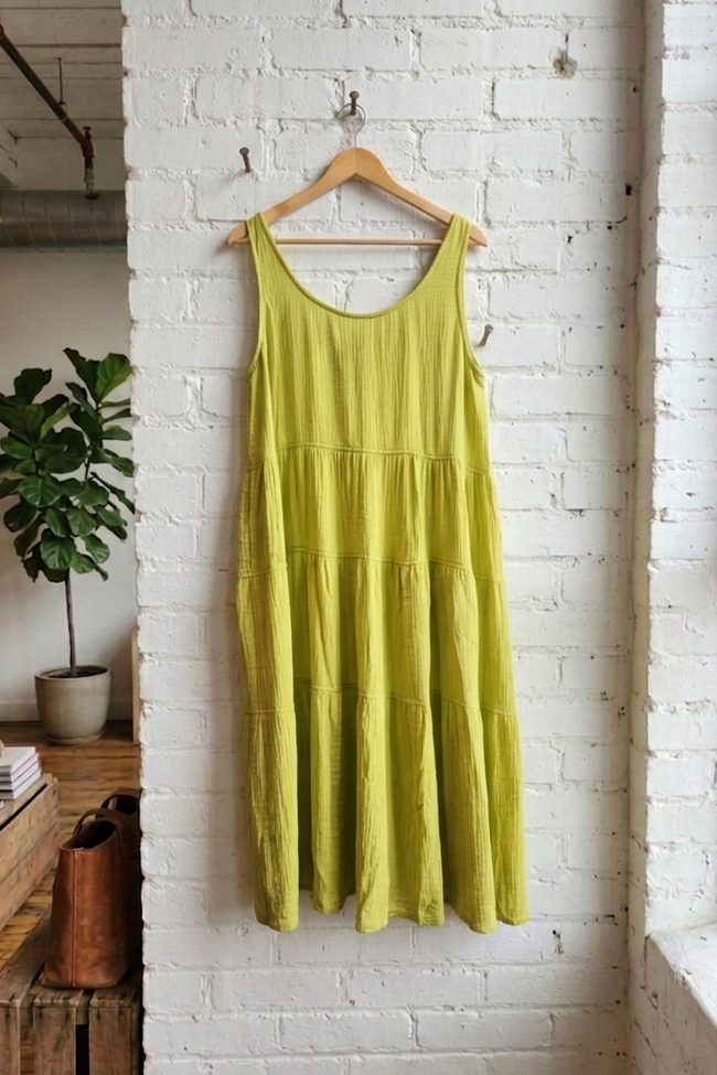 Green dress hanging on a wooden hanger against a white brick wall.