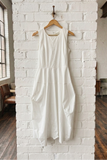 White dress hanging on a wooden hanger against a white brick wall.