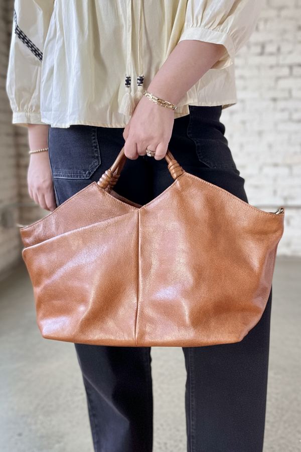 Person holding a brown leather bag indoors with a neutral background
