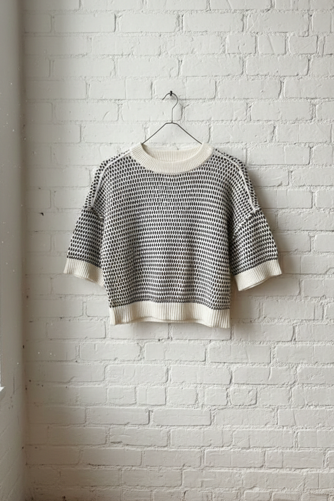 Black and white patterned sweater on a hanger against a white brick wall.