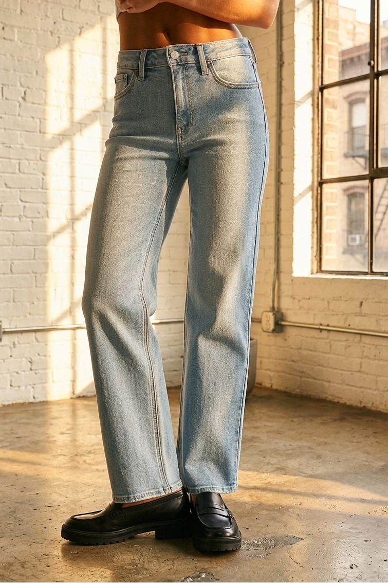 Person wearing light blue jeans standing in a sunlit room with large windows.