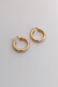 A pair of polished gold-tone hoop earrings with a thick, rounded tubular design and post-back closures, displayed on a clean, light gray surface.