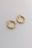 A pair of polished gold-tone hoop earrings with a thick, rounded tubular design and post-back closures, displayed on a clean, light gray surface.